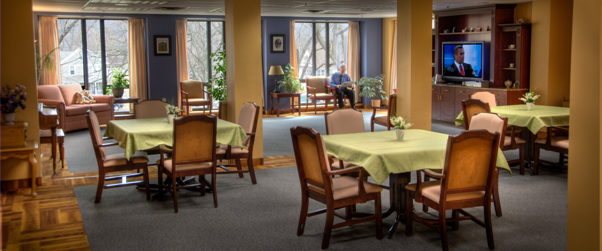 Community lounge with couches, entertainment console, and several dining tables at the Good Shepherd Fairview Home